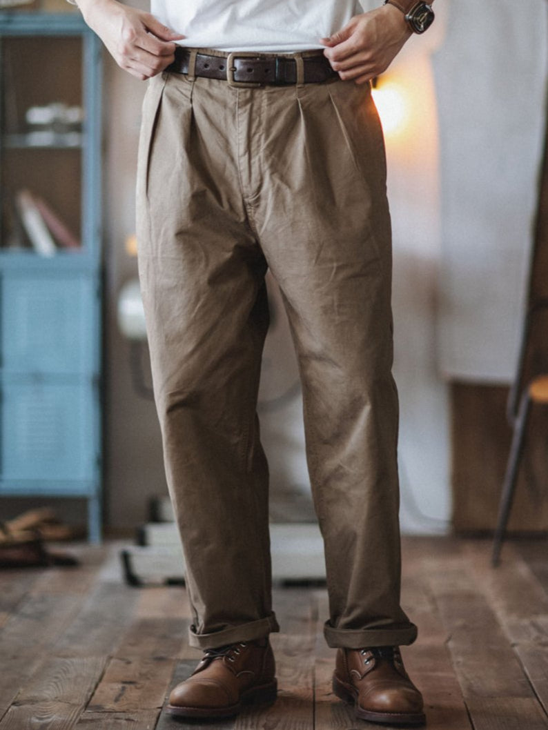 A person wearing straight fit chino pants with a relaxed fit, standing in a room with wooden flooring and a variety of furniture in the background.